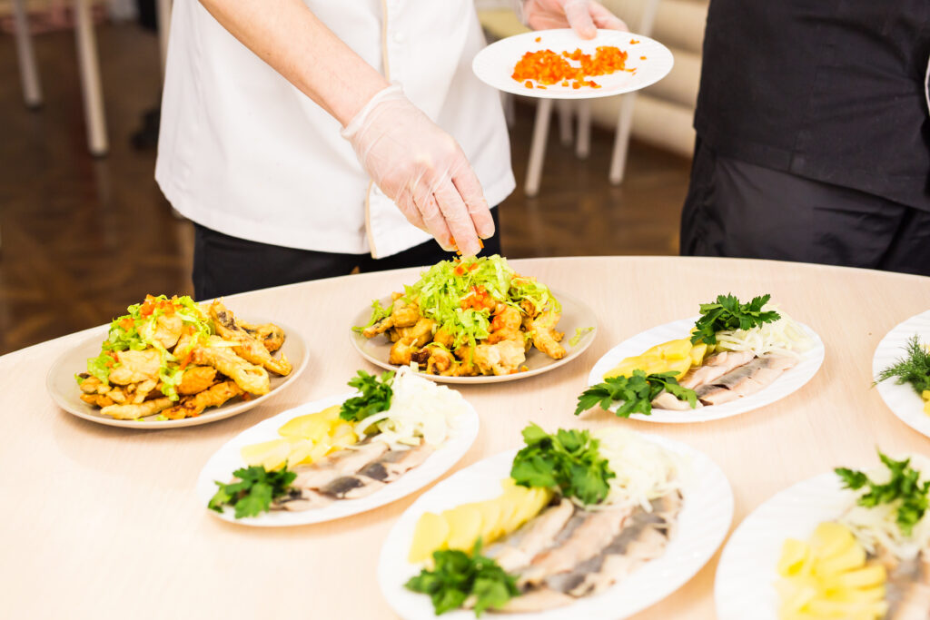 Köche richten frisch zubereitete Teller mit Fisch, Gemüse und Kräutern an – Einblick in die Küche von Aubergine & Zucchini in Meckenheim
