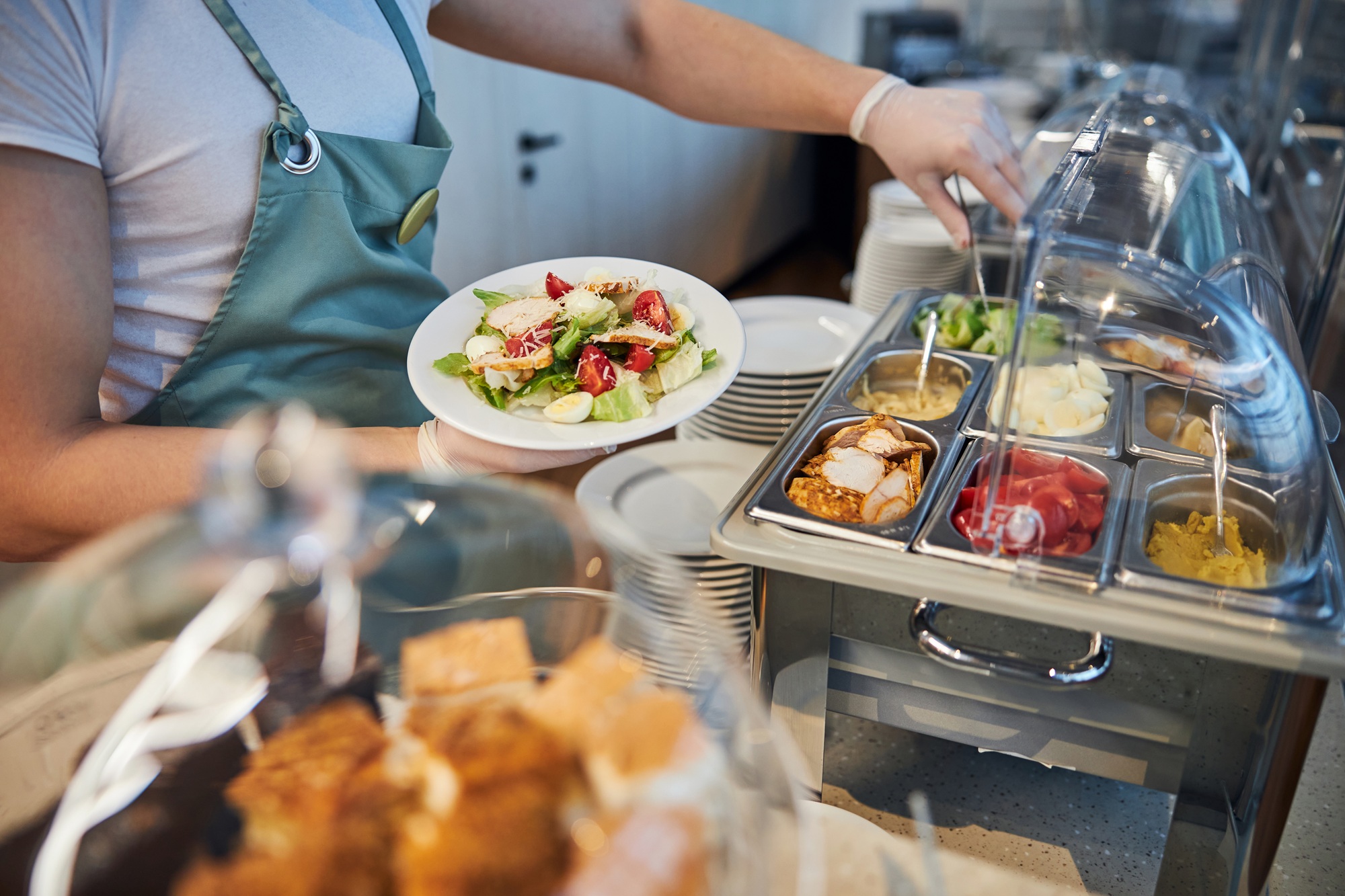Lebensmittelverschwendung im Kitacatering vermeiden: Ein Kita-Kind isst einen realistisch portionierten, bunten Gemüseteller vollständig auf, im Hintergrund die Zentralküche von Aubergine & Zucchini in Meckenheim